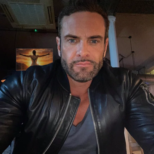 PHNX Lex in a black leather jacket, with the ASCEND album artwork on the wall behind
